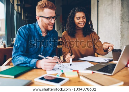 Positive caucasian young man and cheerful dark skinned student watching together funny webinar during e-learning on modern laptop computer connected to wireless 4G internet sitting in university Royalty-Free Stock Photo #1034378632