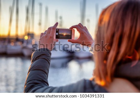 young woman take a photo of the sunset in the port on a mobile phone smartphone, travel photography, social networks