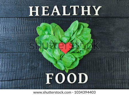 I love a healthy lifestyle. Green leaves in the shape of heart and red small heart on a black wooden background. Vegan food.