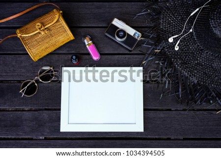 Minimal styled flat lay isolated on original white paper and dark wood background. Woman desk top view with accessories: hat, handbag, sunglasses, vintage photo camera, headphones, notebook, cosmetics