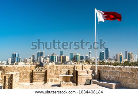 Bahrain Flag with skyline of Manama at Bahrain Fort. A UNESCO World Heritage Site in the Middle East Royalty-Free Stock Photo #1034408164
