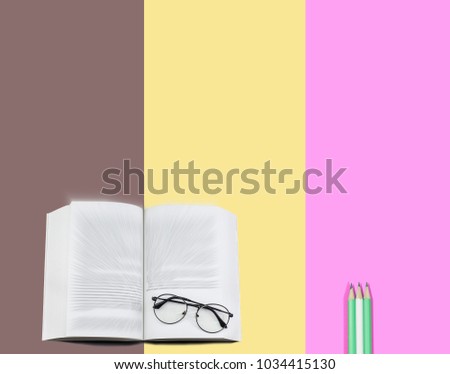 Glasses on text book and pencils on brown, yellow and pink background. Education concept.