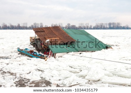  A wooden house and boat disappearing in the ice blocks of deeply frozen Danube river.
