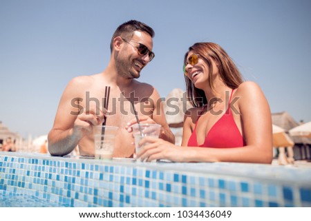 Young happy couple drinking a lemonade in the swimming pool,having fun together.