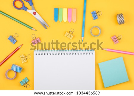 Multicolored set of pencils and blank notepad and office supplies  laying on yellow background top view. Creative set for hobby