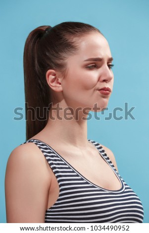 Beautiful female three-quarters portrait. isolated on blue studio backgroud. The young emotional boring woman is standing.The human emotions, facial expression concept. Profile view. Trendy colors