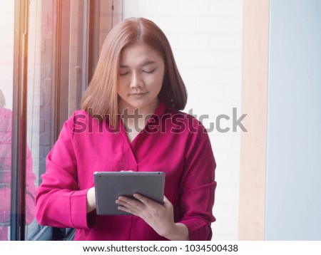 Worker women smile and happy with her job. Asian women stand beside the window and use tablet with her job. Women is looking and touching on the tablet. 