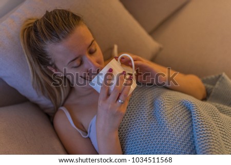 Upset young woman suffering from influenza at home. Young woman drinking tea during fever. Flu.Woman Caught Cold. Headache. Virus. Flue. Woman sick in bed with temperature drinks hot