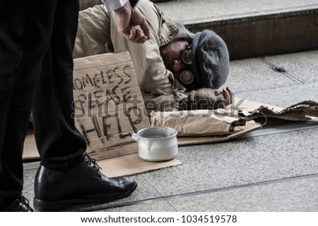 Businessman with suit donate some money in the metal bowl to help homeless man and he is sleeping on street or walkway in the city.