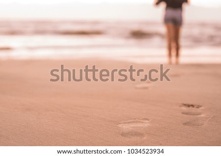Woman walking on the beach, footprints in the sand.