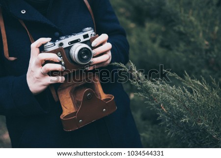 Woman’s hands holding retro photo camera and taking photo outdoor. Lifestyle concept with autumn nature on background. Close-up. Tone photo