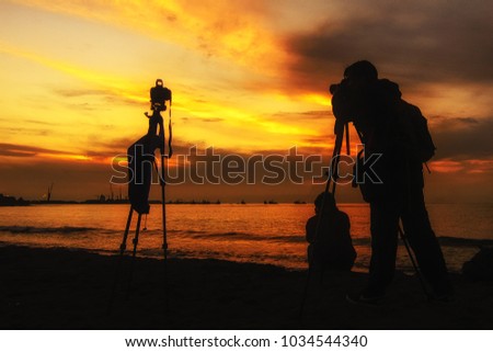 Silhouette Photographer take photo dramatic sunset sky on beach in twilight.