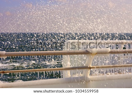 Metallic fence in the ice with wave foam splash on the northern coast of the Black Sea. Odessa, Ukraine.Odessa, Ukraine.