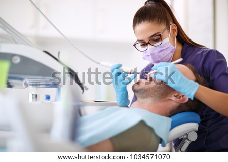 Female dentist drilling tooth to male patient in dental chair Royalty-Free Stock Photo #1034571070