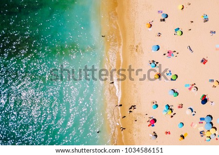 Aerial View From Flying Drone Of People Crowd Relaxing On Beach In Portugal Royalty-Free Stock Photo #1034586151