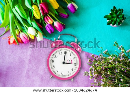 Change to daylight saving time photo of pink alarm clock from above as flatlay with a bunch of tulips and flowers in front of colourful background in spring