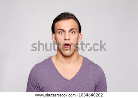 emotion, advertisement and people concept - Handsome young man on grey background looking at camera. Portrait of laughing young man in pockets leaning against grey wall. guy is surprised