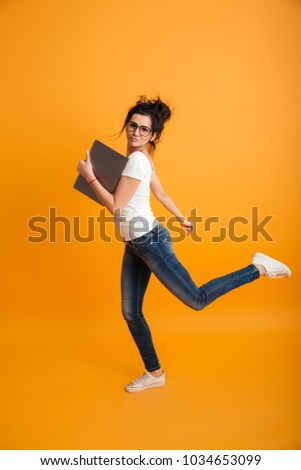 Image of cheerful young woman running isolated over yellow background using laptop computer looking camera.