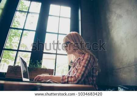 Concept of coworking via the internet. Low angle side profile half-faced view photo of concentrated minded pensive woman in casual checkered shirt, she is surfing the internet, sitting at the table