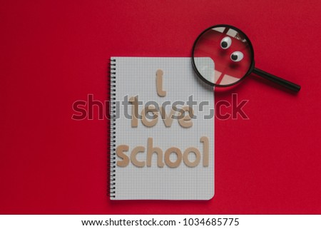 Animated magnifying glass looking to a notebook with "I love school" wooden lettering on it. Red Background.