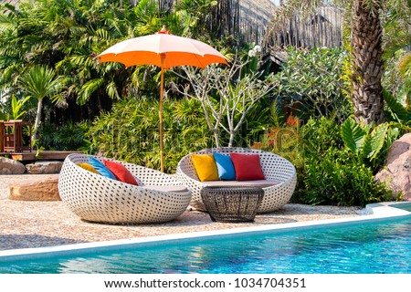 Beautiful beach with swimming pool, coconuts palm trees, rattan daybeds and umbrella in a tropical garden near sea, Thailand