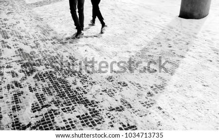 Legs of two people walking down the snowy sidewalk arcade  in motion blur in black and white