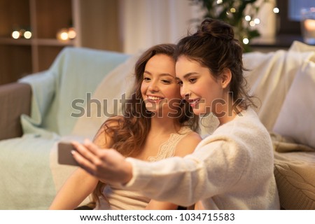 friendship, hygge and technology concept - happy female friends or teenage girls taking selfie by smartphone at home