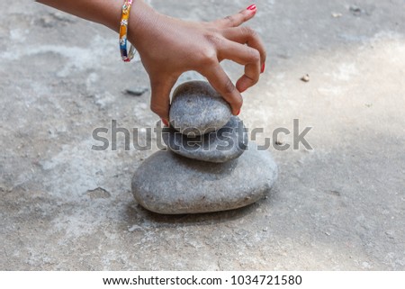 A young girl child seen playing and constructing stone pyramid using pebbles 
 and with her tiny fingers