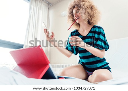 Woman working from home reading messages on her phone sitting on her bed