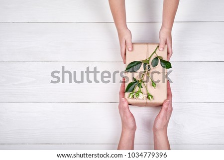 Son giving gift box with flowers to mum, top view. Holidays, present, childhood concept. Close up of child and mother hands with gift box on white background. Mothers day, Womens day (March 8), Easter
