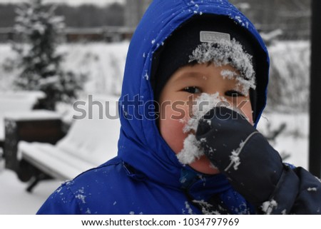 Cheerful little boy in blue clothing eating the snow, face in the snow