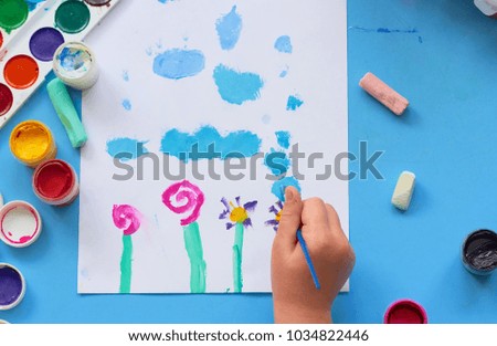 
The child draws on white paper with colored paints.