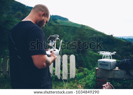 Man connecting smartphone to remote controller for making photos and shooting videos of beautiful tea plantations of asia mountains from modern drone during summer expedition standing on high hill