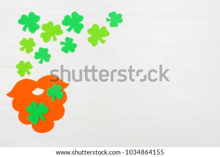 St. Patrick's Day theme colorful horizontal banner. Orange leprechaun hand made beard and green shamrock leaves on white wooden background with copy space. Felt craft elements for greeting card.