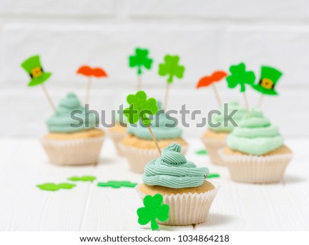 St. Patrick's Day theme colorful horizontal banner. Cupcakes decorated with green buttercream and craft felt decorations in form of leprechaun hat, mustache and shamrock leaves on white background.