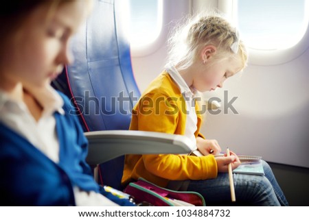Adorable little girls traveling by an airplane. Child sitting by aircraft window and drawing a picture with colorful pencils. Traveling abroad with kids.