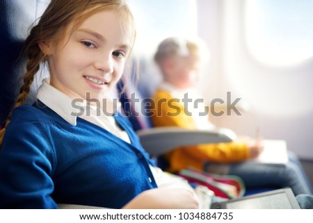 Adorable little girls traveling by an airplane. Child sitting by aircraft window and drawing a picture with colorful pencils. Traveling abroad with kids.