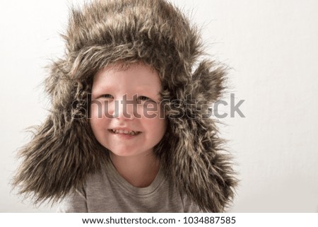 Happy child playing at home. The funny guy put on a warm fur hat and admires himself. Close-up. Portrait with emotions.