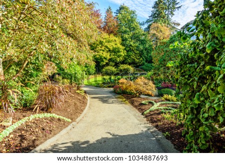 Queen Elizabeth Park, Vancouver BC, Canada.
Asphalt walkway in a city park with flower beds, green trees and bushes on a summer day with blue sky and white clouds.