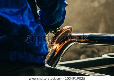 Metal polishing with a hand sander with a polishing disk. Toned image. Hand grinder workflow creation stainless pipe. working process with the sparks Royalty-Free Stock Photo #1034919025