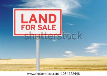 Land for sale sign against empty field and blue sky