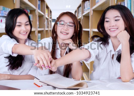 Three high school students joining hands together before studying in the library