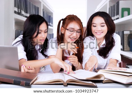 Picture of three female students studying together while sitting in the library 