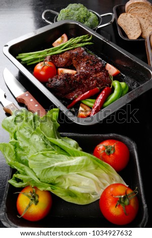 fresh glazed baked big beef meat rib chunk under sweet sauce with lettuce broccoli tomatoes hot chili pepper pink peppercorn different spices on black wooden table