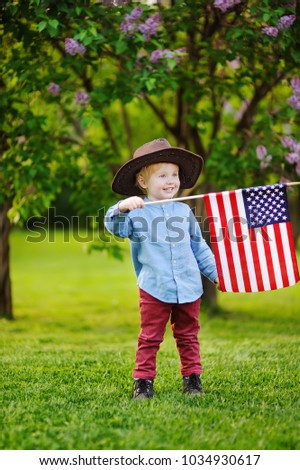 Cute toddler boy holding american flag in beautiful park. Independence Day concept.