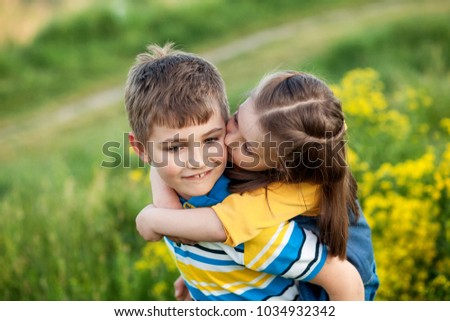 Happy children 5-8 years old, brother and sister, friends, outdoors in summer in a field of blooming yellow flowers, the boy rolls on the back of the girl