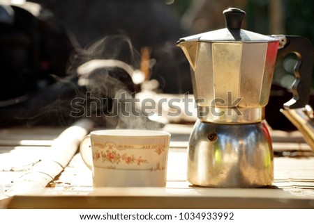Coffee steamer and a cup with steam on bamboo table in a morning