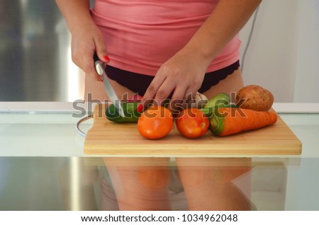 Woman is cutting fresh vegetables on a wooden cutting board.