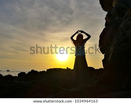 A girl make heart symbol on sunset at seaside