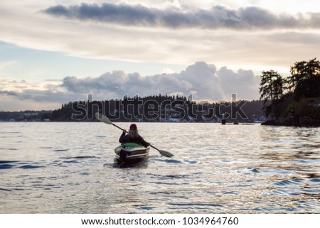 Adventurous girl is kayaking on an inflatable kayak during a vibrant winter sunset. Taken in Indian Arm, Deep Cove, Vancouver, BC, Canada. Concept: Adventure, Holiday